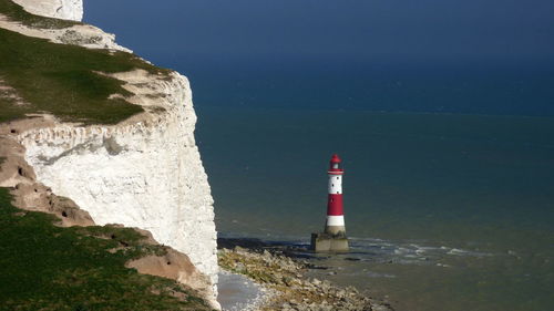 Lighthouse at sea shore against clear blue sky