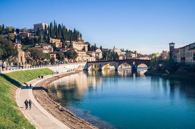 Bridge over river by buildings against clear sky