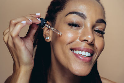 Close-up portrait of young woman applying make-up against wall