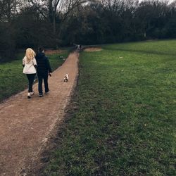 Rear view of couple with dog walking on footpath in park