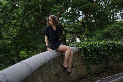 Full length of young woman sitting on retaining wall