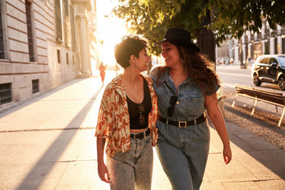 Optimistic young women in stylish clothes smiling while walking on street of madrid, spain