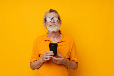 Portrait of young woman holding trophy against yellow background