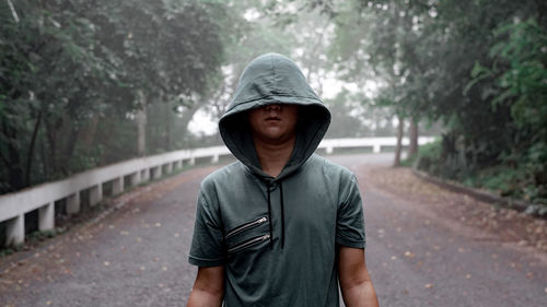 Man with hooded shirt standing on road against trees