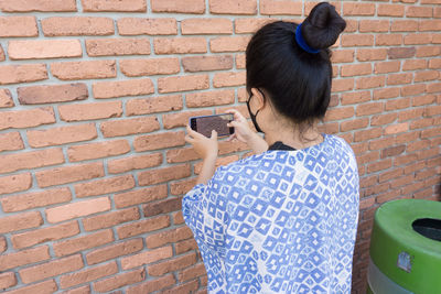 Side view of young woman standing against brick wall