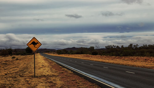 Kangaroo sign by empty road against cloudy sky