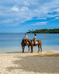 Couple sitting on horse at beach