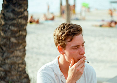 Young man smoking cigarette at beach