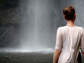Rear view of woman standing in front of waterfall