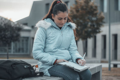 Young woman studying while sitting on bench