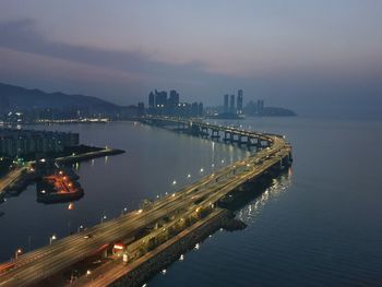 High angle view of illuminated city by river against sky