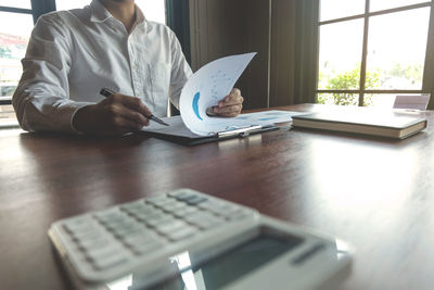 Midsection of man holding paper while sitting on table