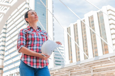 Female engineer holding hardhat while standing in city