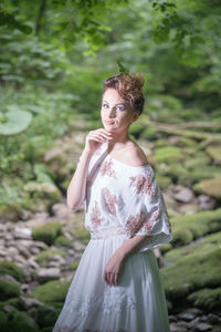 Portrait of young woman standing against trees