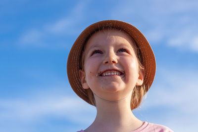 Cute little girl in a straw hat with ice cream on the face after eating on blue sky background. 