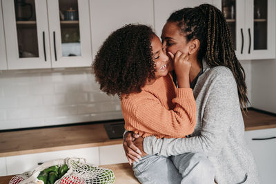 Mother embracing daughter in kitchen at home