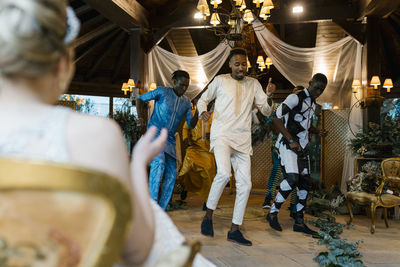 Bridge looking at groom dancing with friend in wedding at banquet