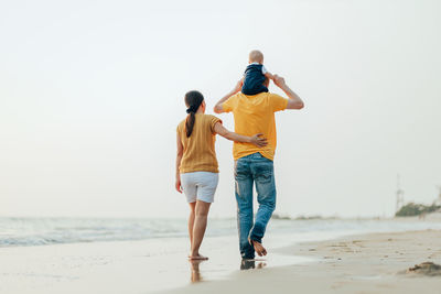 Rear view of family on beach against sky