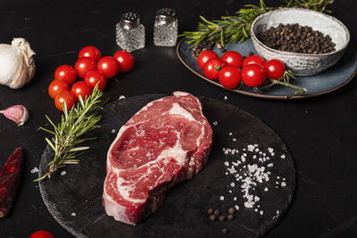 At the table, a raw beef entrecote with rosemary, salt and pepper on a round slate.