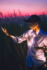 Young man holding illuminated string light while standing on field during dusk