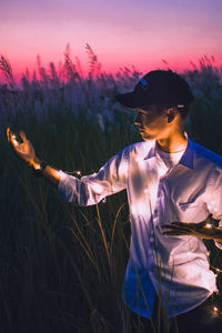 Young man standing on field against sky during sunset