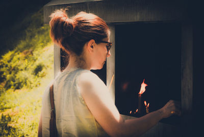 Young woman lighting candle in shrine