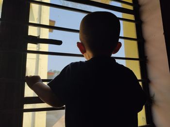 Rear view of boy standing by window at home