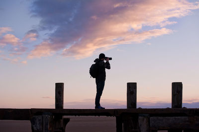 Silhouette of woman standing against sky at sunset