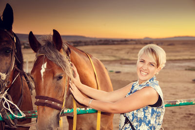 Portrait of smiling young woman holding brown horse on field