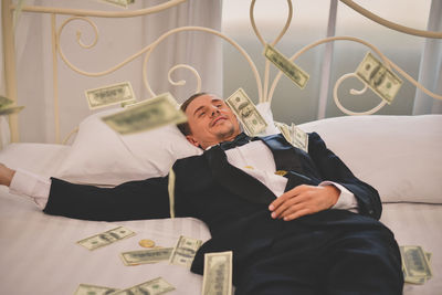 High angle view of mid adult man with money lying on bed at home