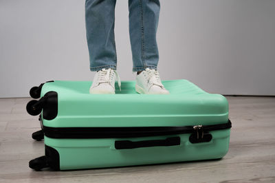 Low section of woman standing on suitcase against wall