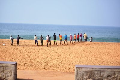 People standing on beach against clear sky