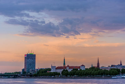 Buildings at waterfront against cloudy sky