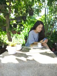 Young woman using mobile phone while sitting on tree