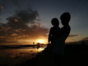 Silhouette people on beach against sky during sunset