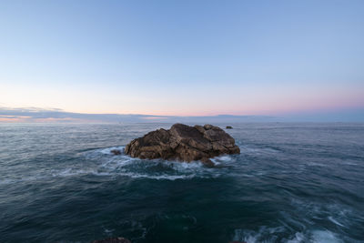 Rocks in sea against sky during sunset