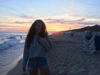 Woman standing at beach against sky during sunset