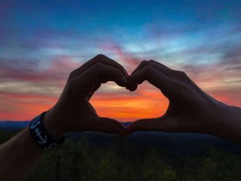 Close-up of hand holding heart shape against sky during sunset