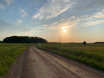 Road amidst field against sky during sunset