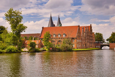 View of buildings by river against cloudy sky