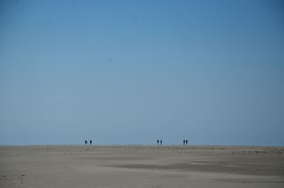 Scenic view of silhouettes on beach against clear blue sky