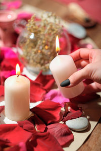 Female hand holding burning candle over rose petals, stones and herbs. aura readings magical rituals