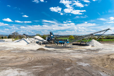 Conveyor over heaps of gravel on blue sky at an industrial cement plant.