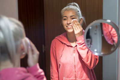 Smiling young woman applying make up in bathroom