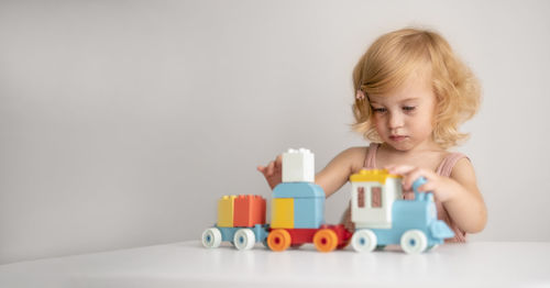 Pretty caucasian interested 1,2 year old with blond curly hair playing with colourful wooden toys 