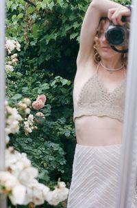 Midsection of woman holding camera while standing by plants