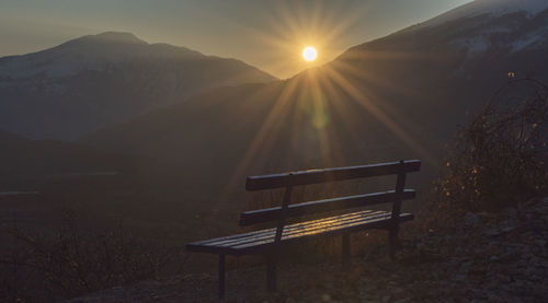 Empty bench on mountain against sky during sunset