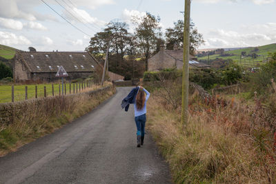 Rear view of man walking on road amidst field