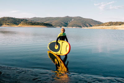 Side view of male surfer in wetsuit standing with yellow sup board and paddle in sea water
