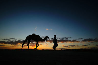 Silhouette people riding horse at sunset
